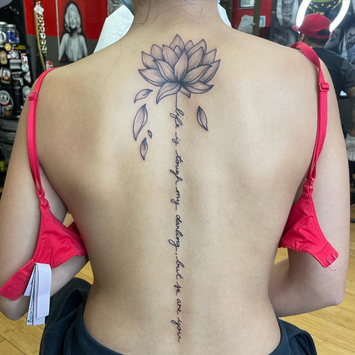 A lotus flower tattoo with a script text stem running down a person's spine.