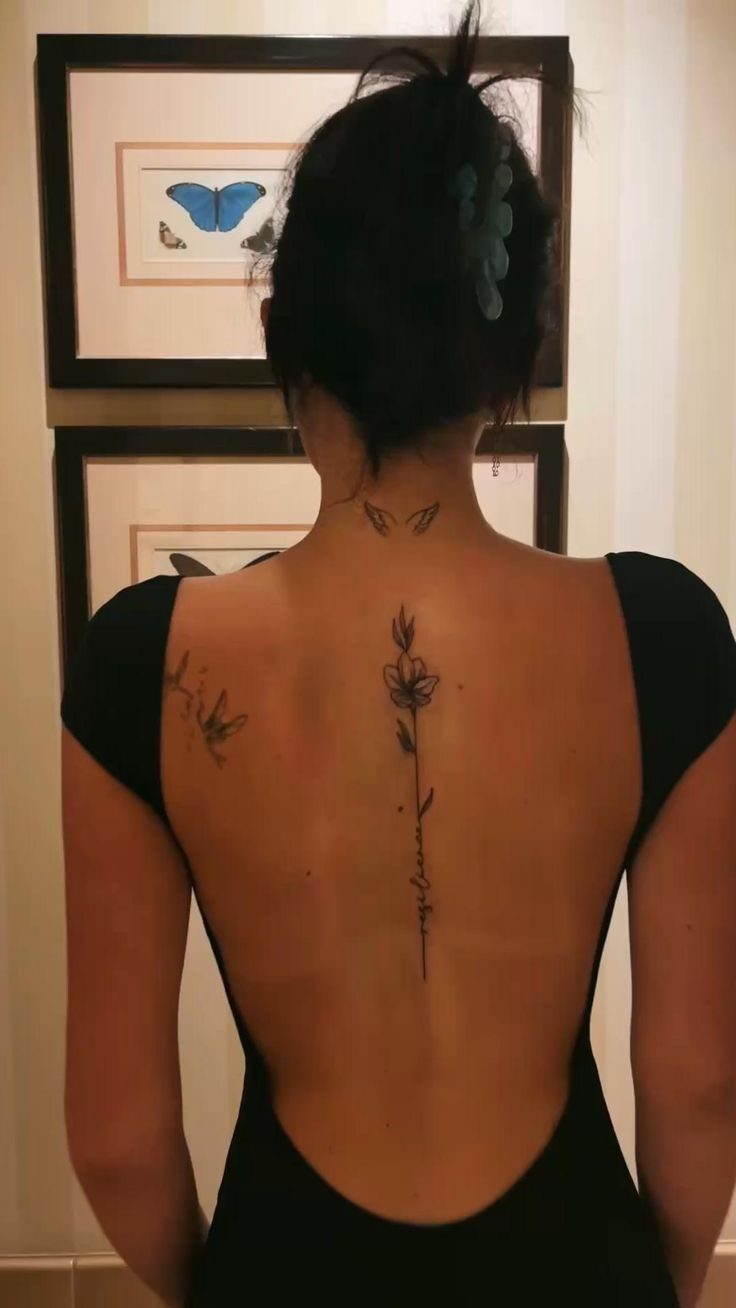 A woman's back featuring a fine line single flower tattoo running down her spine.