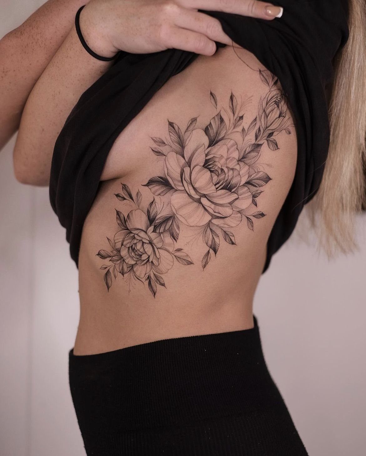 5 Flower Rib Tattoo Ideas for Women and Men 2 Large black and grey peony tattoos covering the side of a person's ribcage.