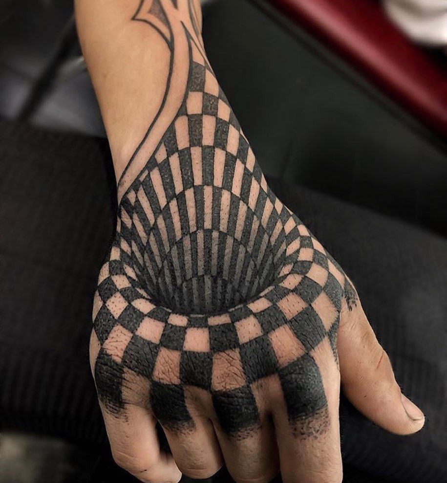 A hand with a black and grey checkerboard tattoo creating a 3D vortex illusion.
