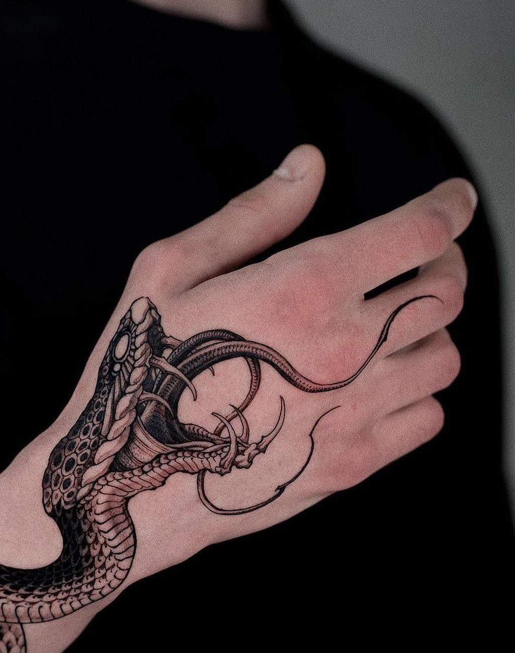 A person's hand featuring a detailed blackwork snake tattoo with scales and a long tongue.
