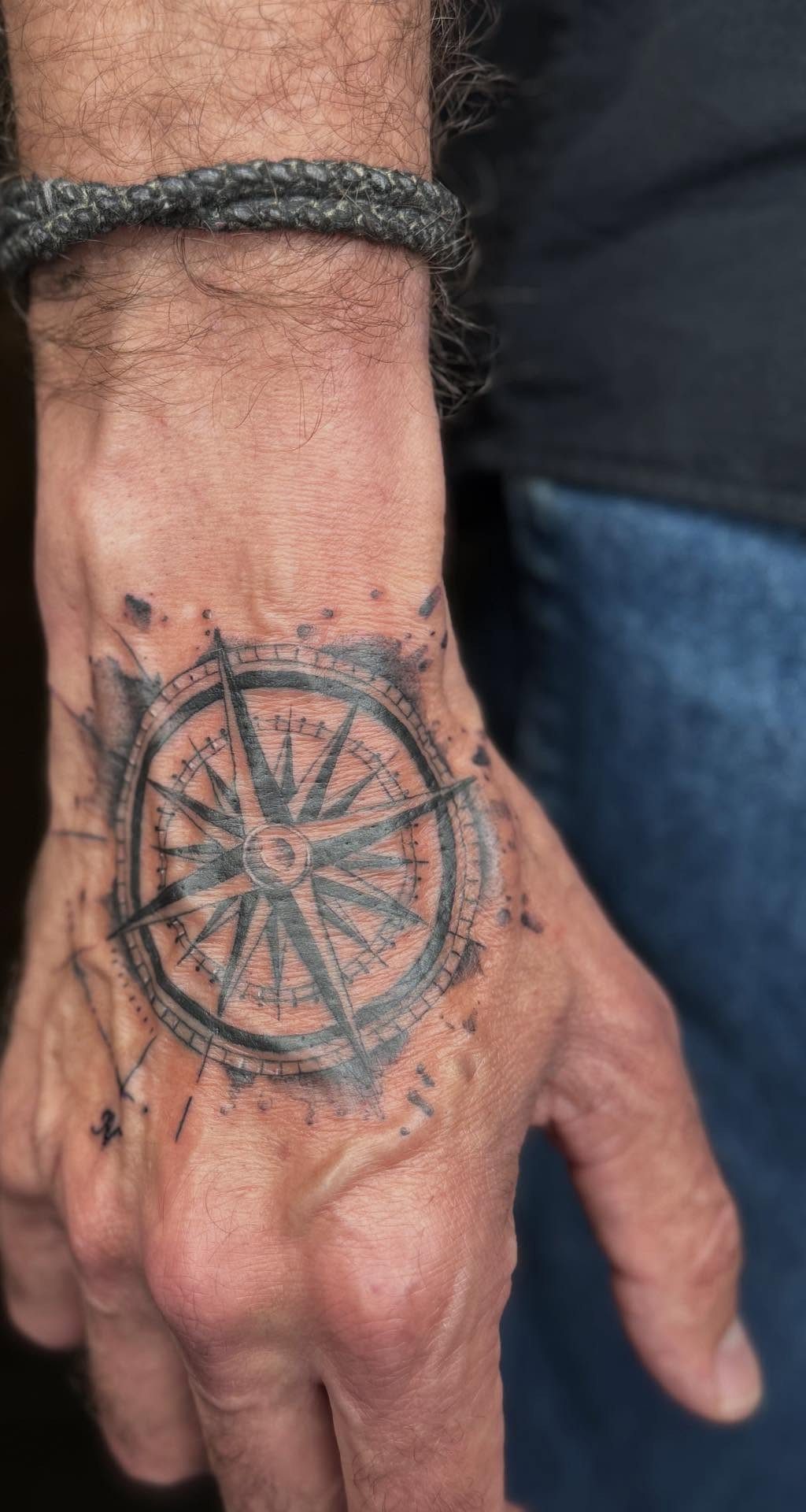 A man's hand featuring a detailed black ink compass rose tattoo on the back.
