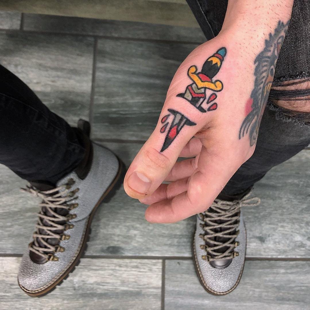 A person's hand displaying a colorful dagger tattoo on the back of the hand.