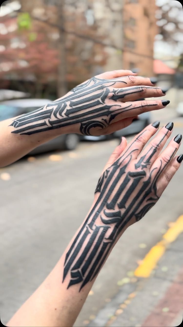 Two hands displaying large blackwork geometric tattoos following the bone structure against an urban background.