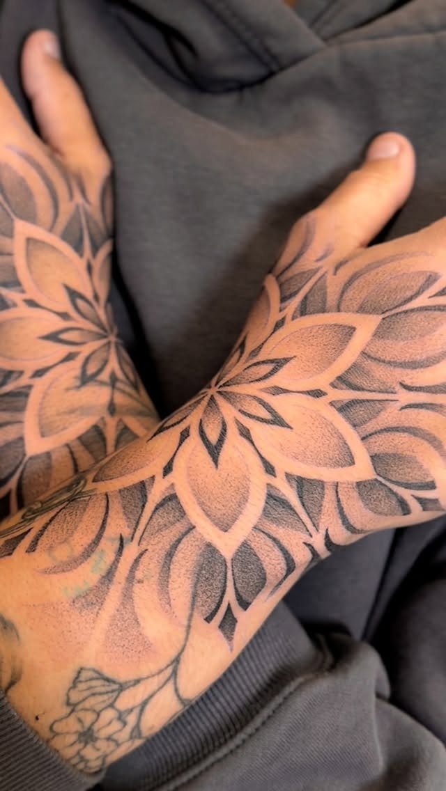Two hands featuring large, symmetrical black ink geometric mandala tattoos on the skin.