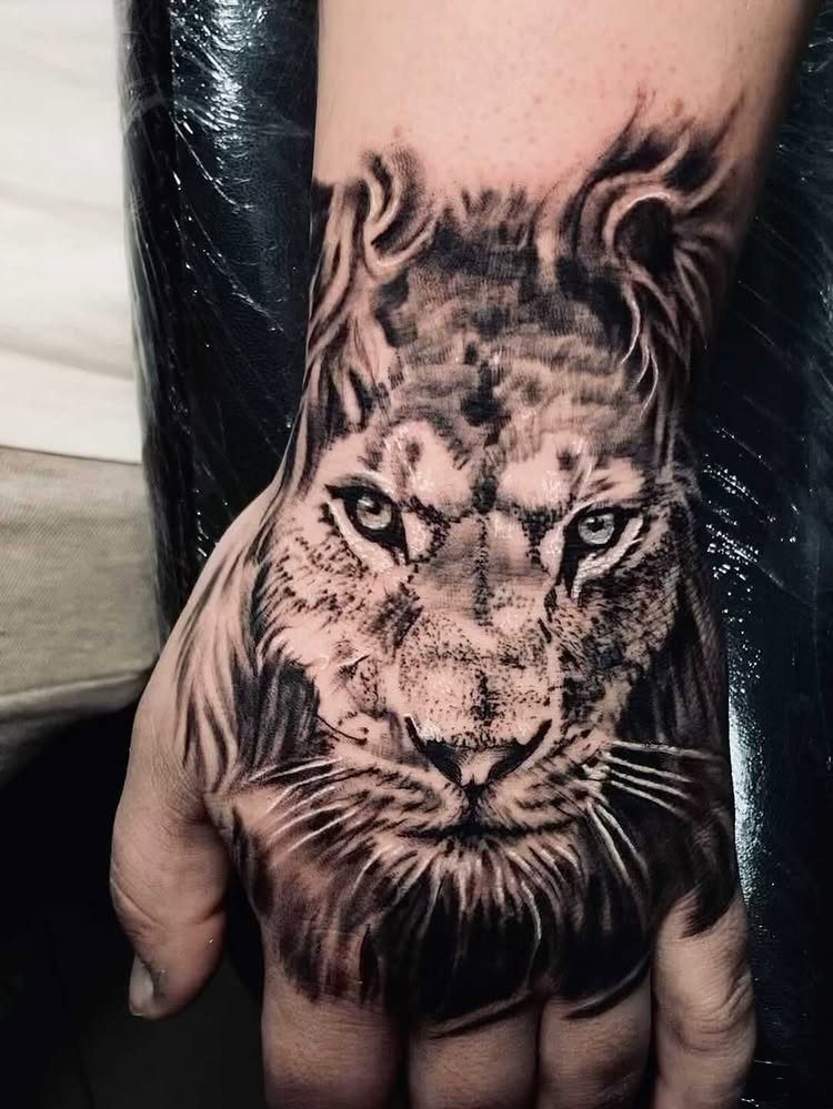 A detailed black and grey lion face tattoo covering a person's hand and wrist.