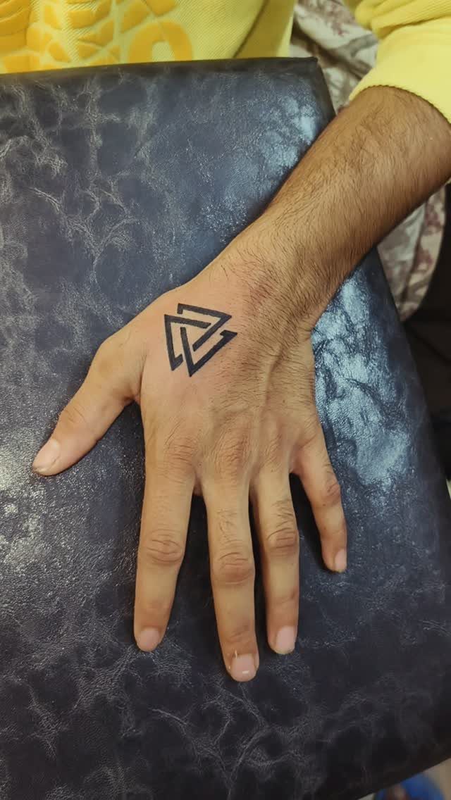 A man's hand displaying a black minimalist geometric triangle tattoo on the back.