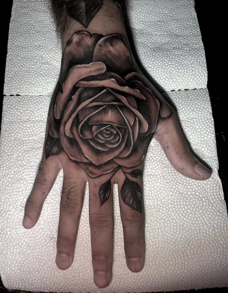 A large black and grey rose tattoo covering the back of a person's hand.