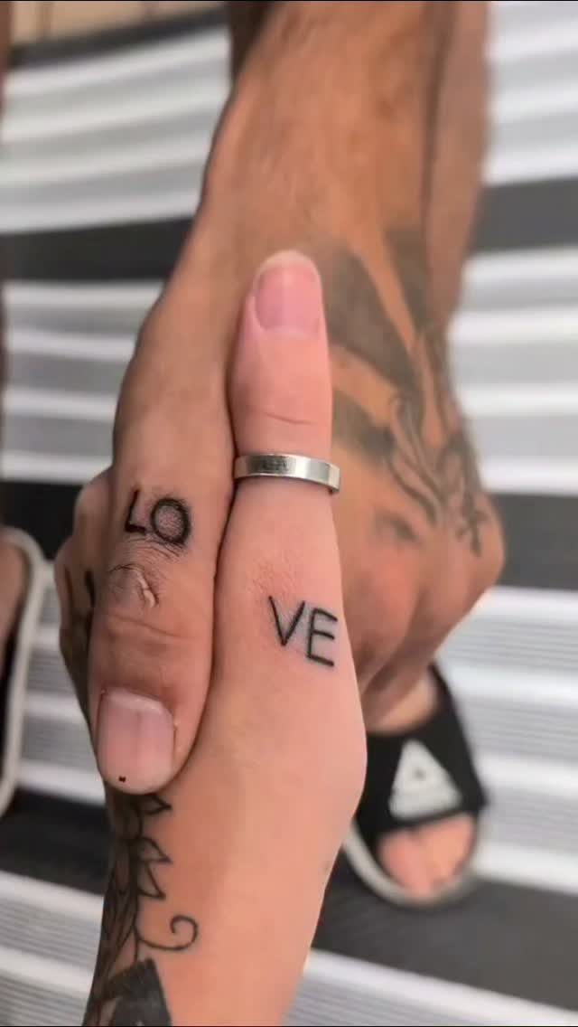 Two hands held together showing finger tattoos that spell out the word LOVE.