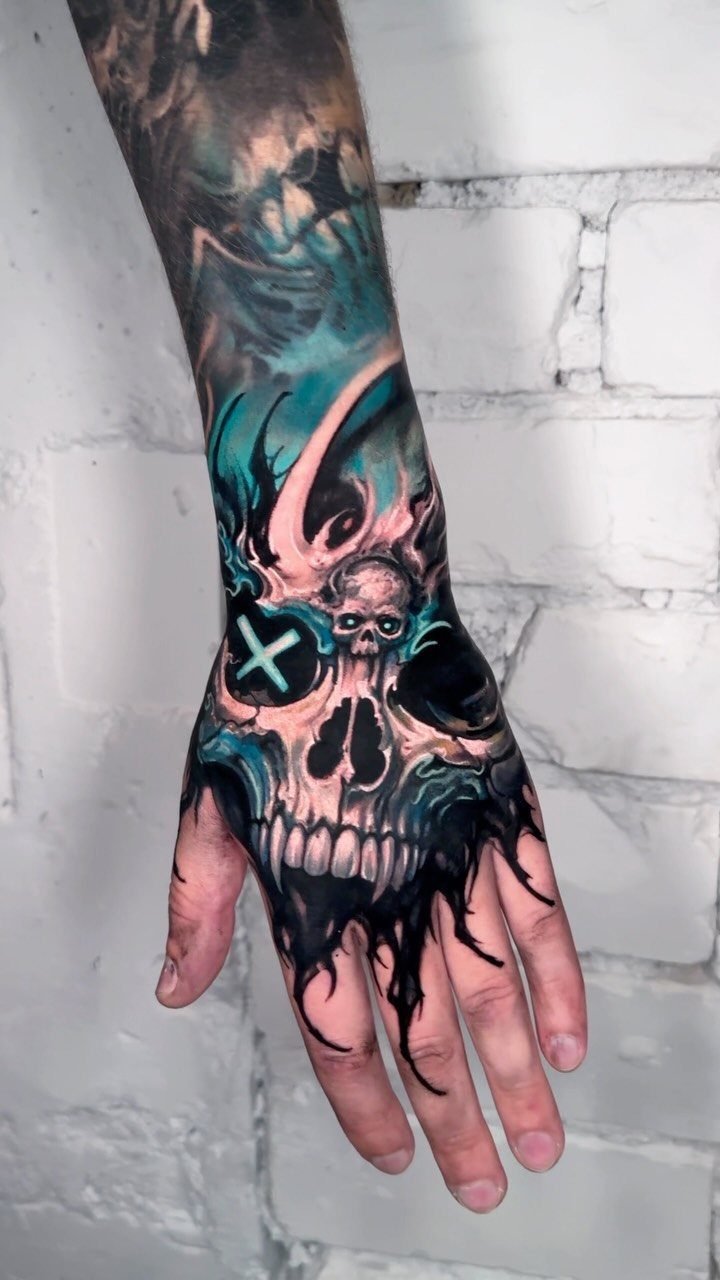 A detailed black and teal skull tattoo covering a person's hand and forearm.