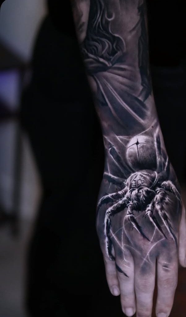 A large black and grey spider tattoo covering a person's hand and forearm.