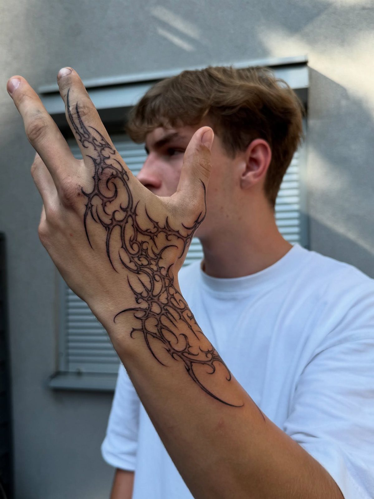 A young man displaying a large black tribal tattoo covering his hand and fingers.