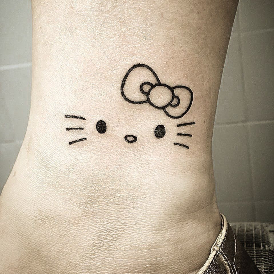 Hello Kitty face line art tattoo on a person's skin near the ankle.