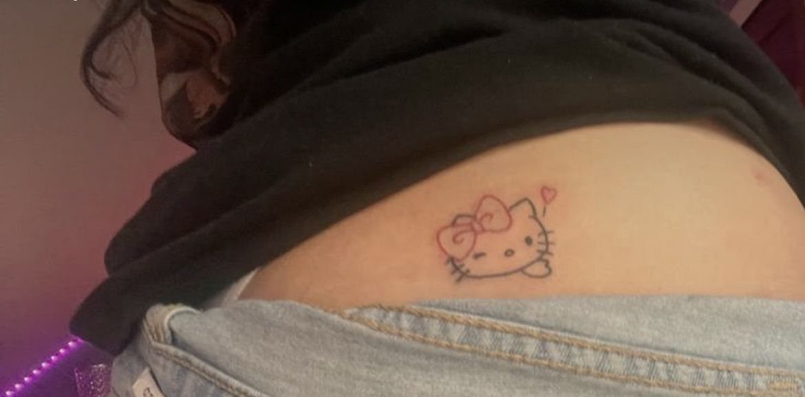 Hello Kitty tattoo with a red bow on a person's lower back above denim jeans.
