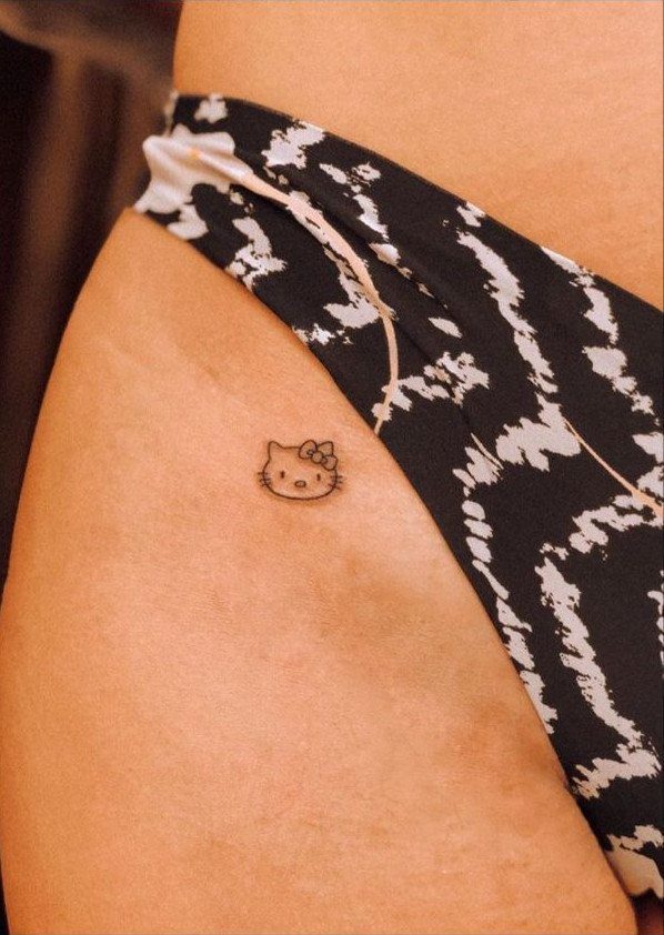A small Hello Kitty outline tattoo located on a person's hip near patterned clothing.