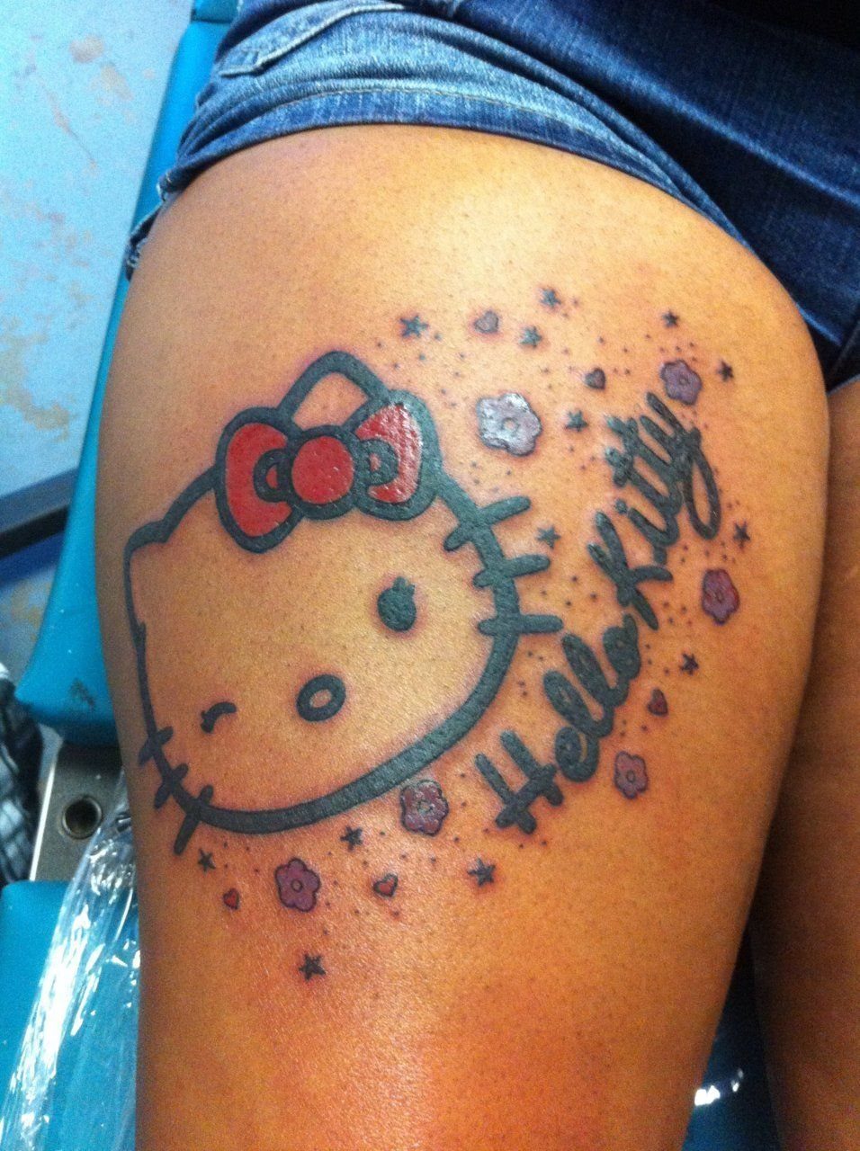 Hello Kitty tattoo with a red bow and stars on a person's thigh.