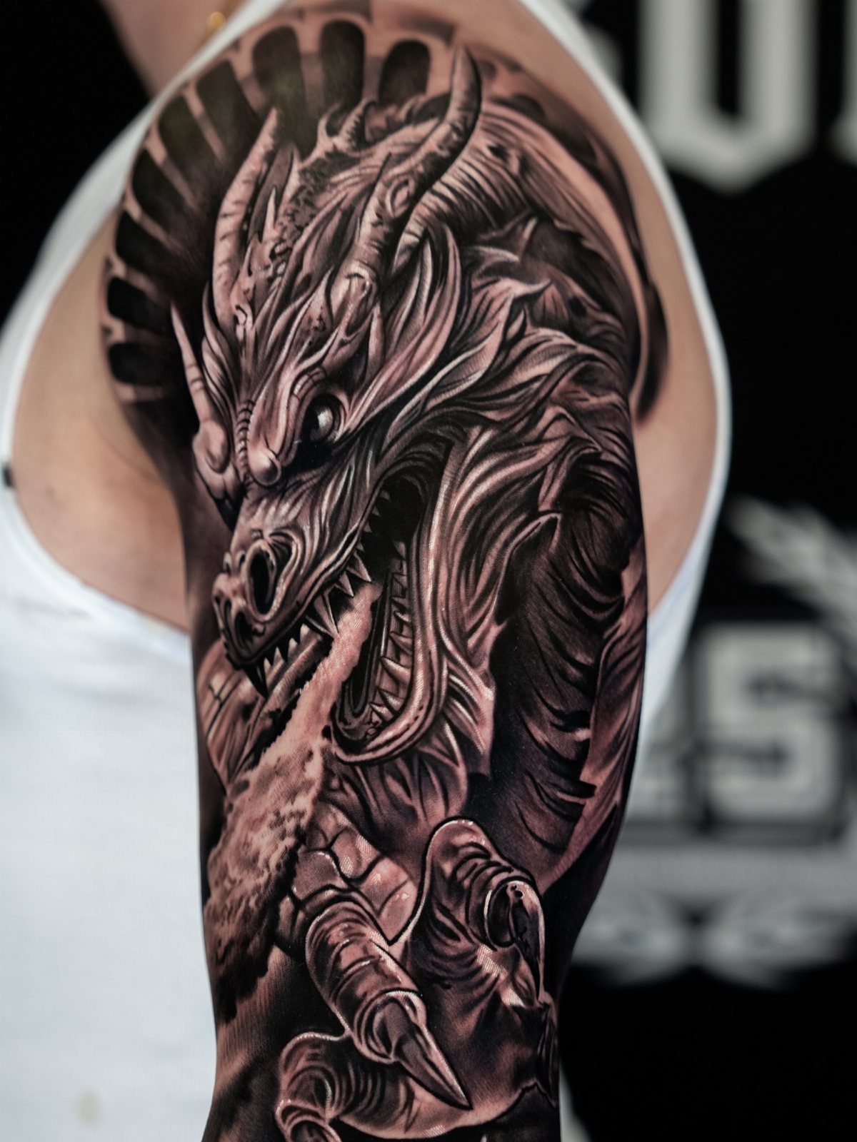 Japanese Dragon Tattoos: 19 Designs With Meaning and Style 4 A detailed black and grey Japanese dragon tattoo covering a person's shoulder and upper arm.