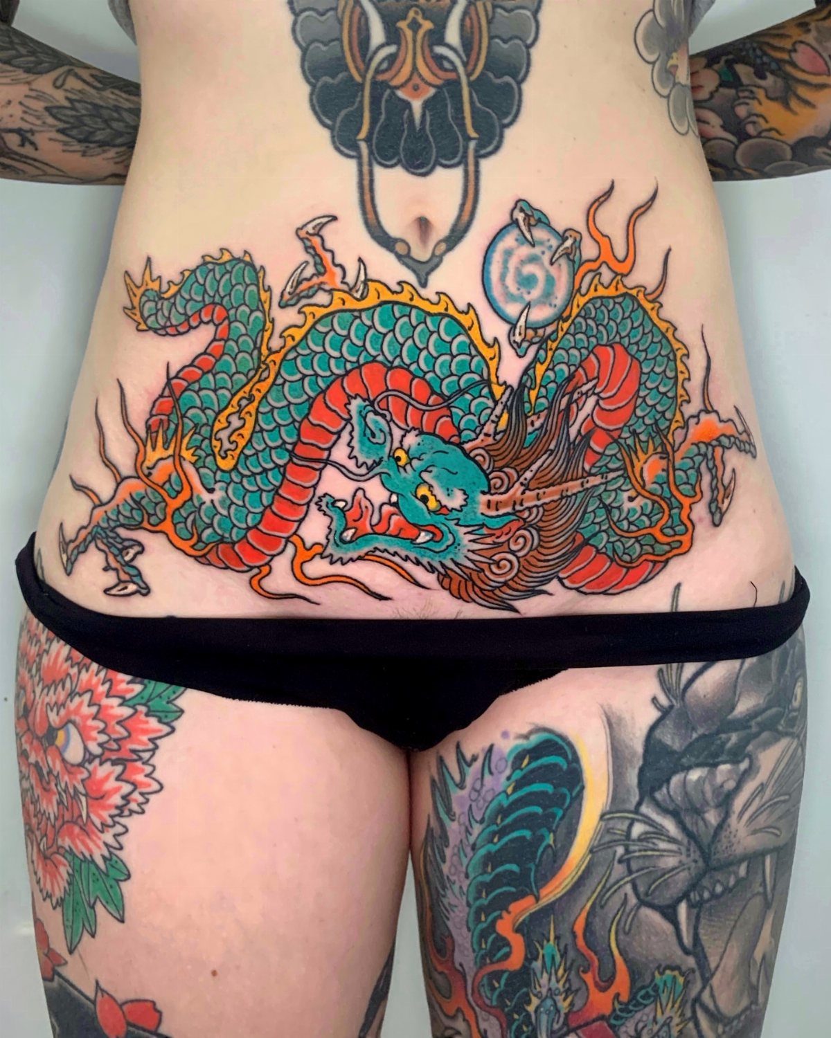 Japanese Dragon Tattoos: 19 Designs With Meaning and Style 9 A vibrant teal and red Japanese dragon tattoo spanning across a person's stomach area.