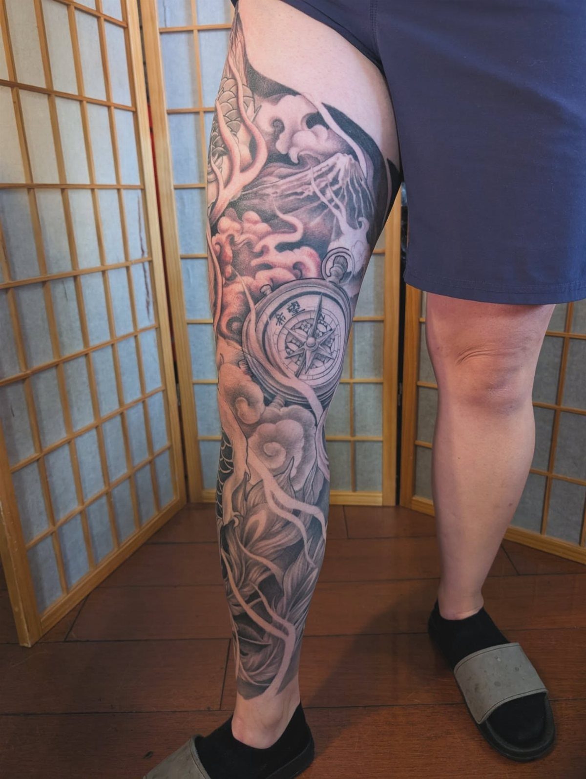 Japanese Dragon Tattoos: 19 Designs With Meaning and Style 15 A large black and grey dragon tattoo covering a person's entire leg with clouds and a compass.