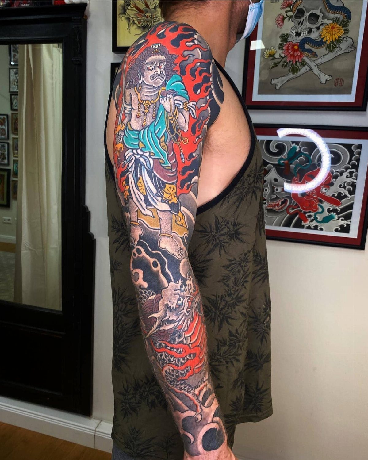 Japanese Dragon Tattoos: 19 Designs With Meaning and Style 11 A man displaying a colorful Japanese sleeve tattoo featuring a deity and a dragon.