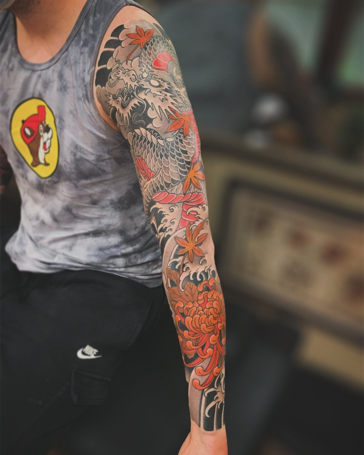 Japanese Dragon Tattoos: 19 Designs With Meaning and Style 12 A detailed Japanese sleeve tattoo featuring a dragon, orange peonies, and red maple leaves on a person's arm.