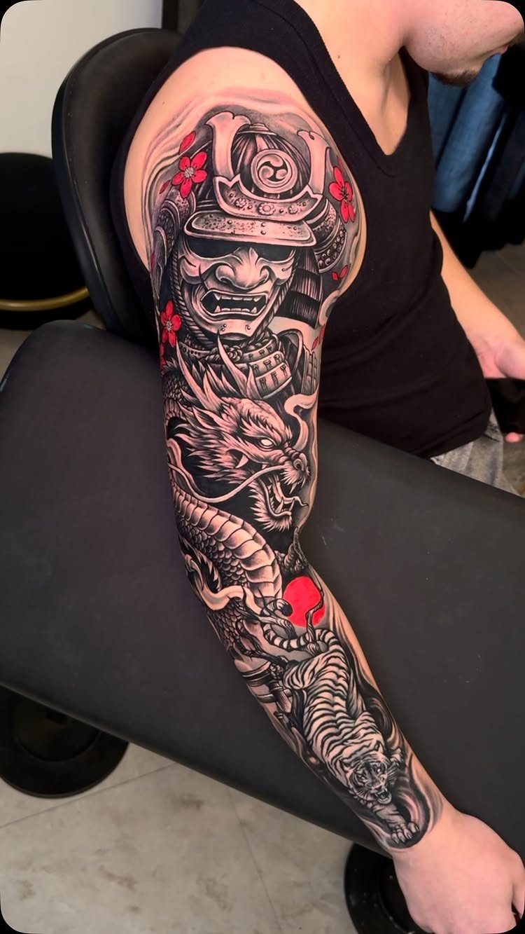 Japanese Dragon Tattoos: 19 Designs With Meaning and Style 17 A detailed black and grey arm tattoo featuring a samurai helmet and a dragon with red flowers.