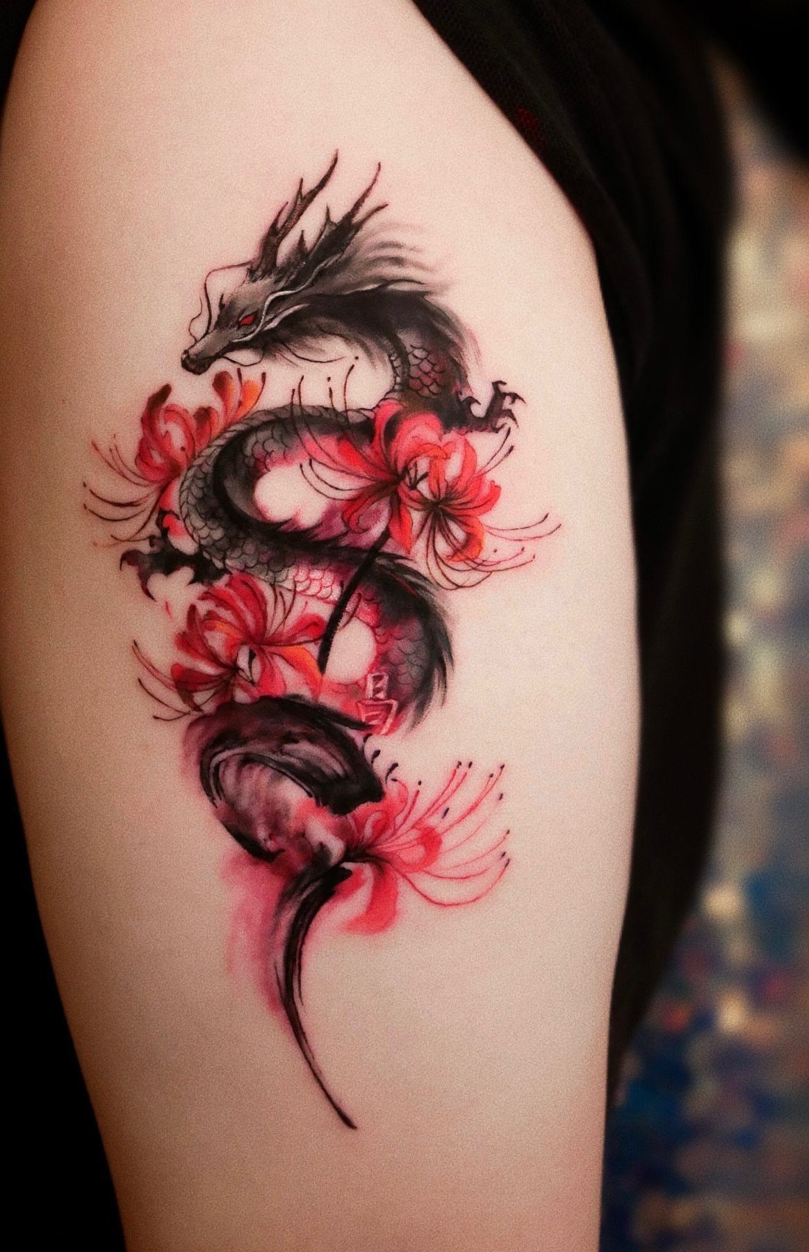 Japanese Dragon Tattoos: 19 Designs With Meaning and Style 14 A black and red dragon tattoo winding through bright red spider lily flowers on skin.