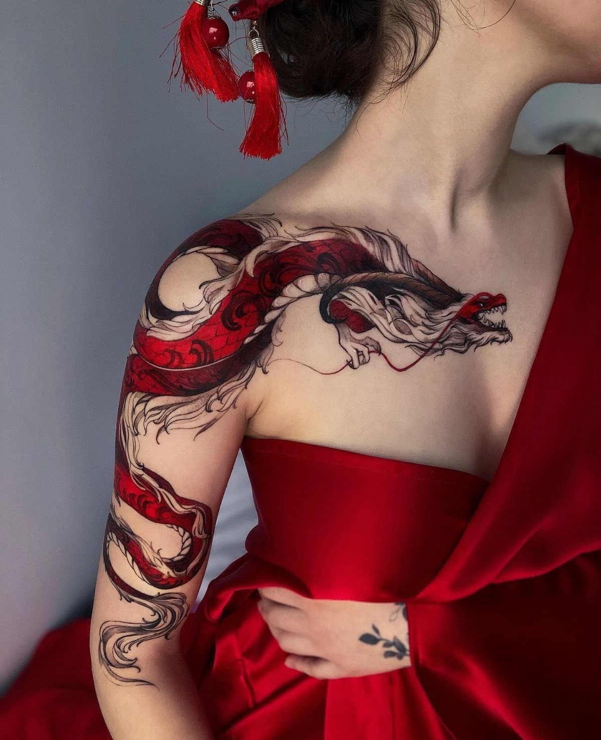 Japanese Dragon Tattoos: 19 Designs With Meaning and Style 13 A large red and black dragon tattoo covering a person's shoulder and upper arm.