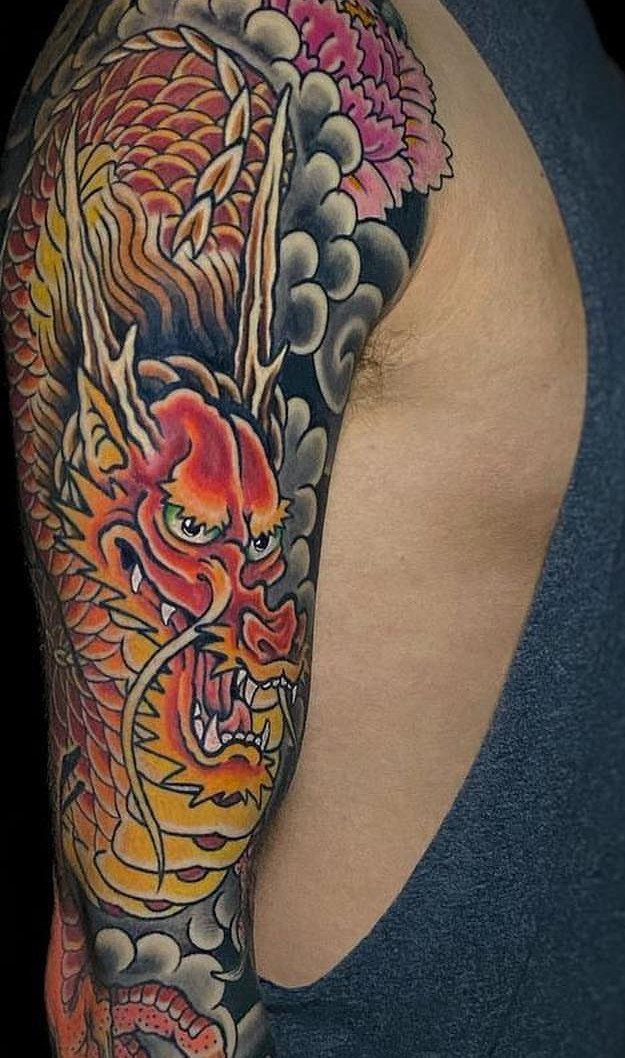 Japanese Dragon Tattoos: 19 Designs With Meaning and Style 5 A vibrant Japanese dragon tattoo with pink peonies on a person's shoulder.