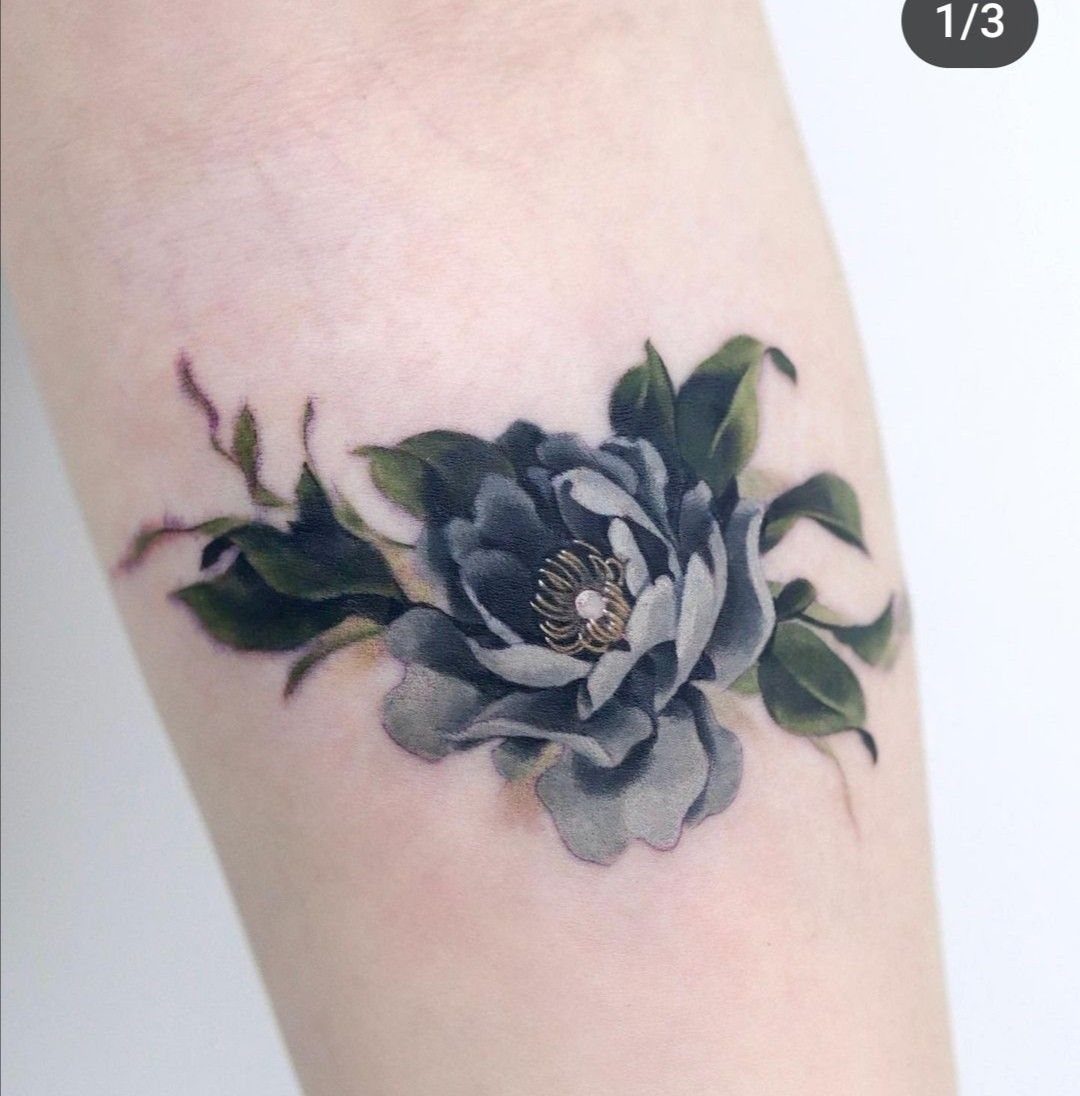 A realistic tattoo of a blooming peony flower with green leaves on human skin.