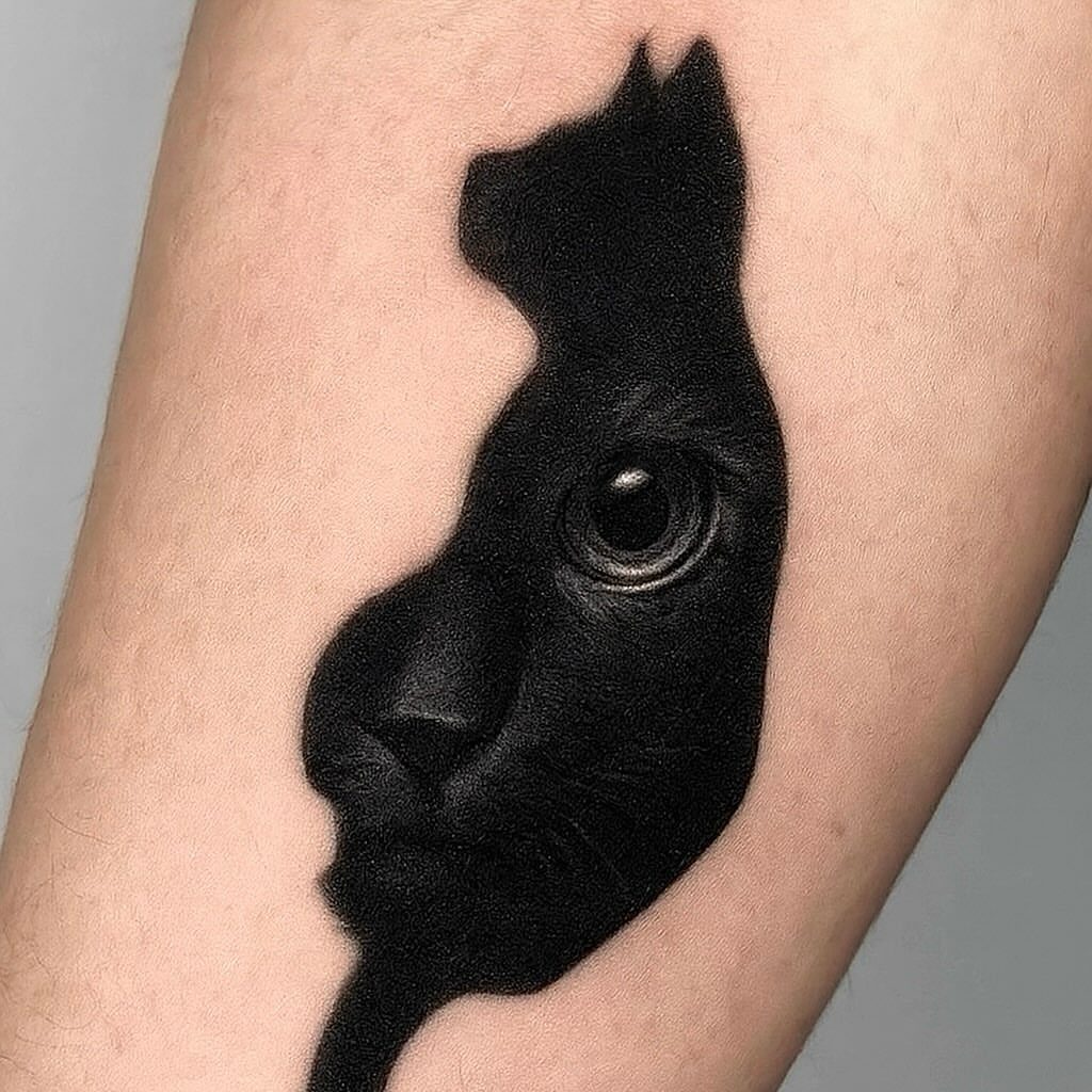 A black ink feline face tattoo featuring a detailed eye on human skin.