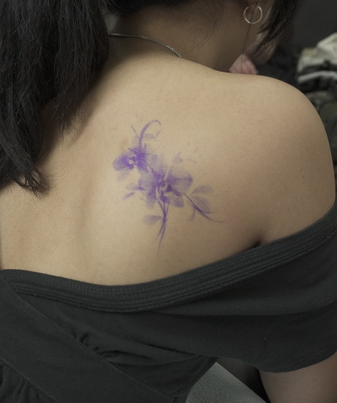 Purple orchid tattoo with soft shading on a person's upper back and shoulder.