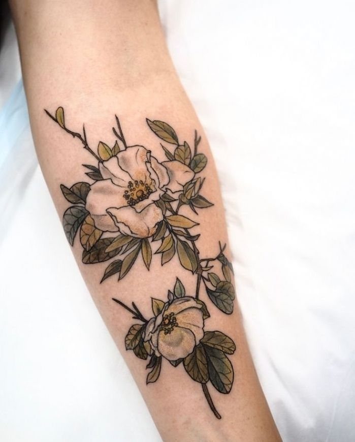 A floral tattoo of white flowers and green leaves on a person's forearm.