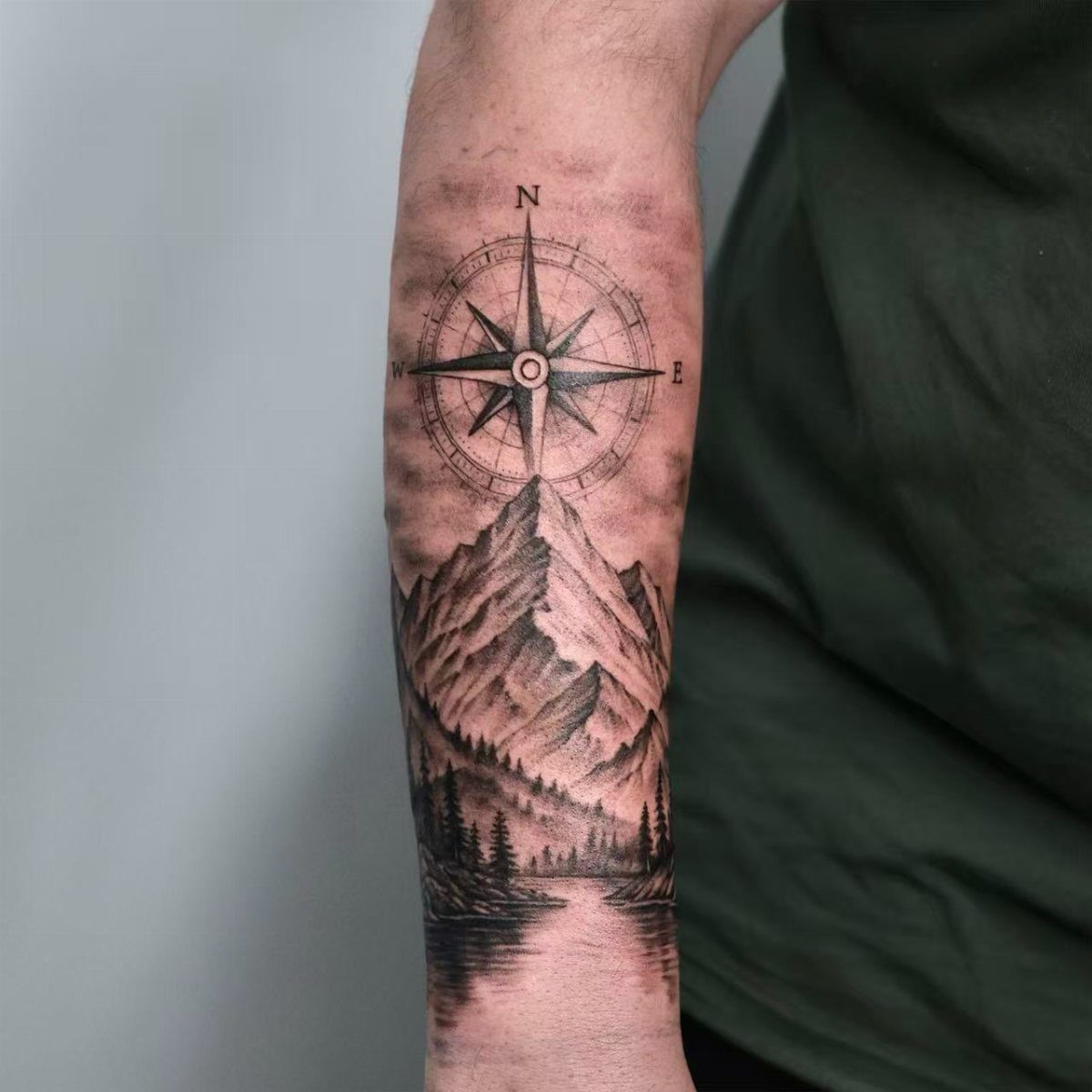 10 Mountain Landscape Tattoo Ideas For Your Next Ink 6 A black and grey forearm tattoo depicting a mountain landscape with a compass rose above the peaks.