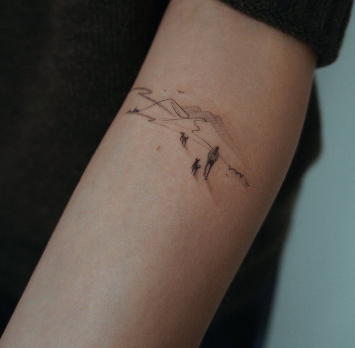 10 Mountain Landscape Tattoo Ideas For Your Next Ink 9 A minimalist black ink mountain landscape tattoo on a person's forearm featuring tiny silhouettes.