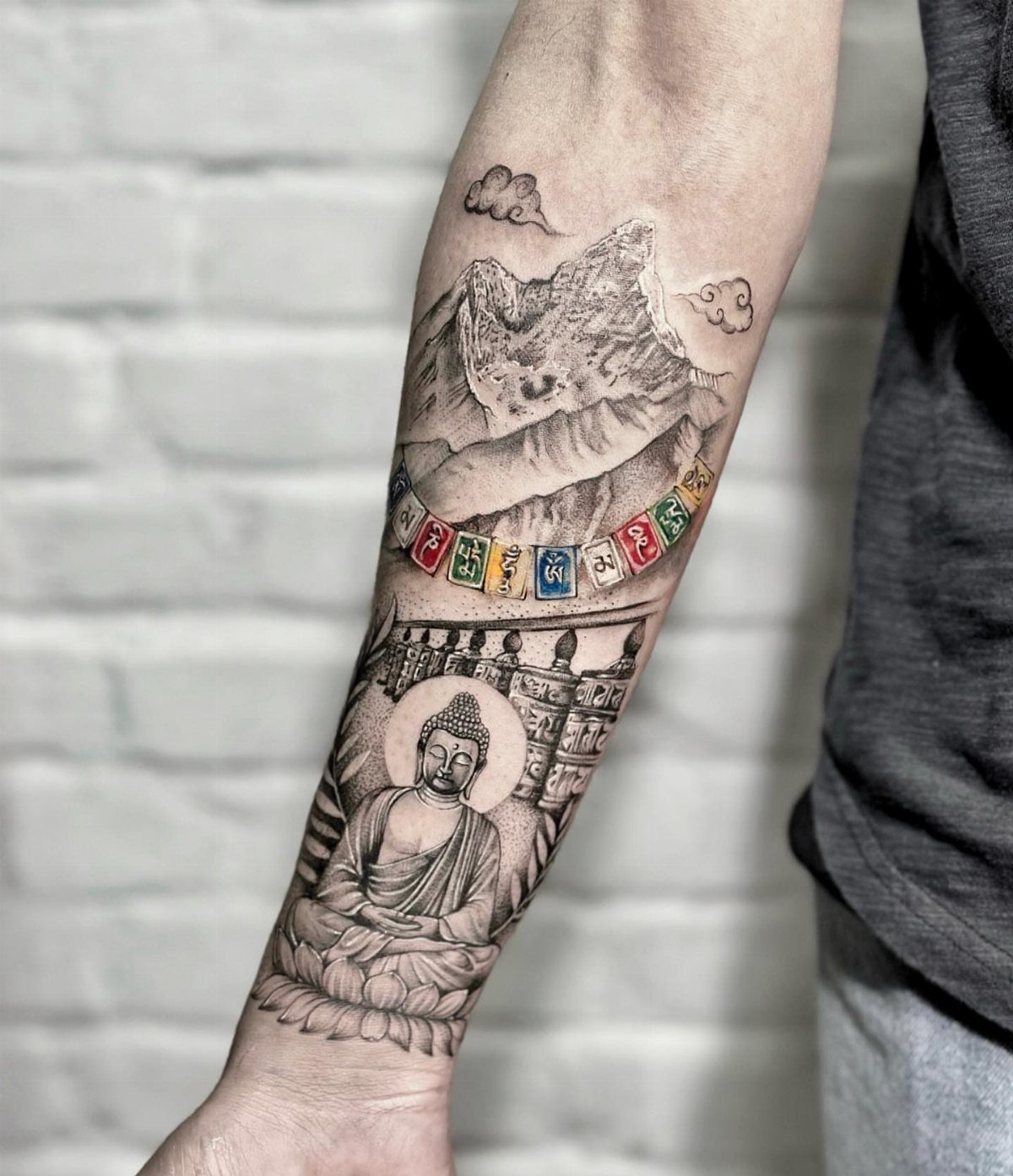 10 Mountain Landscape Tattoo Ideas For Your Next Ink 10 A detailed black and grey forearm tattoo depicting mountains, prayer flags, and a Buddha statue.