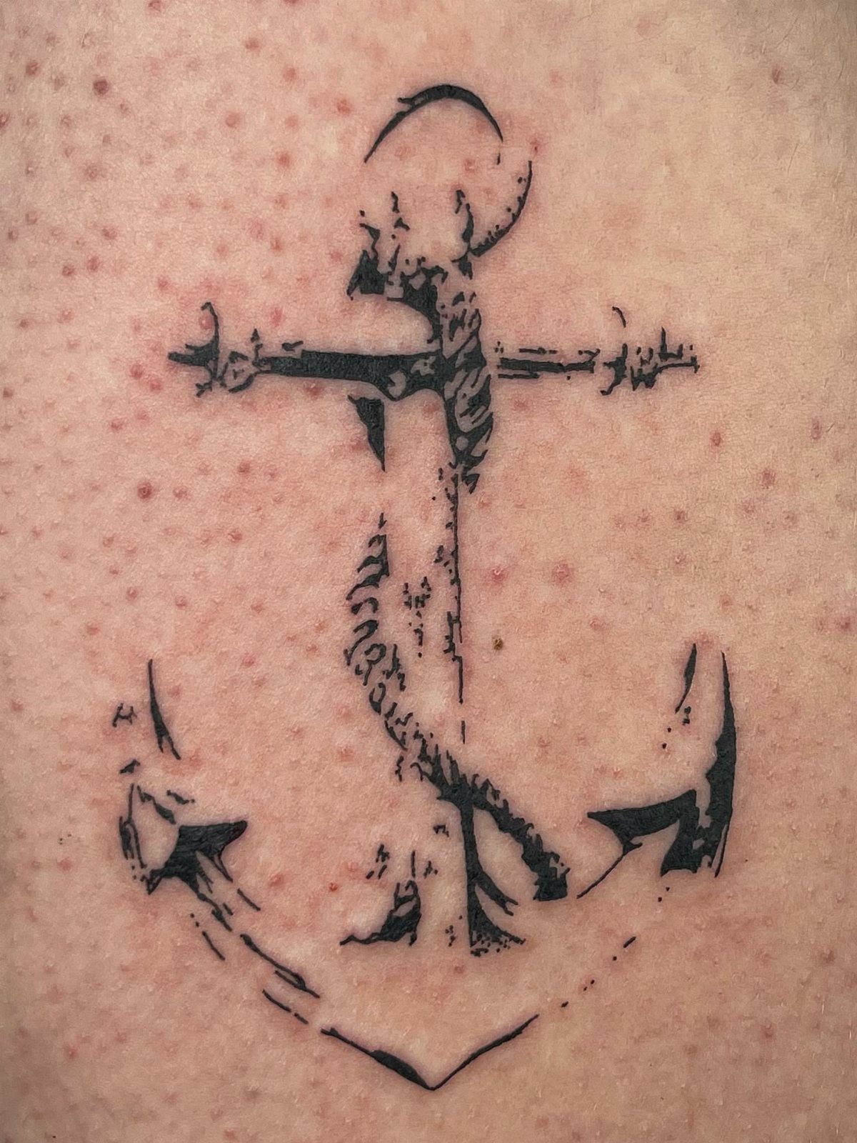 A black ink anchor tattoo with a rope wrapped around it on skin.