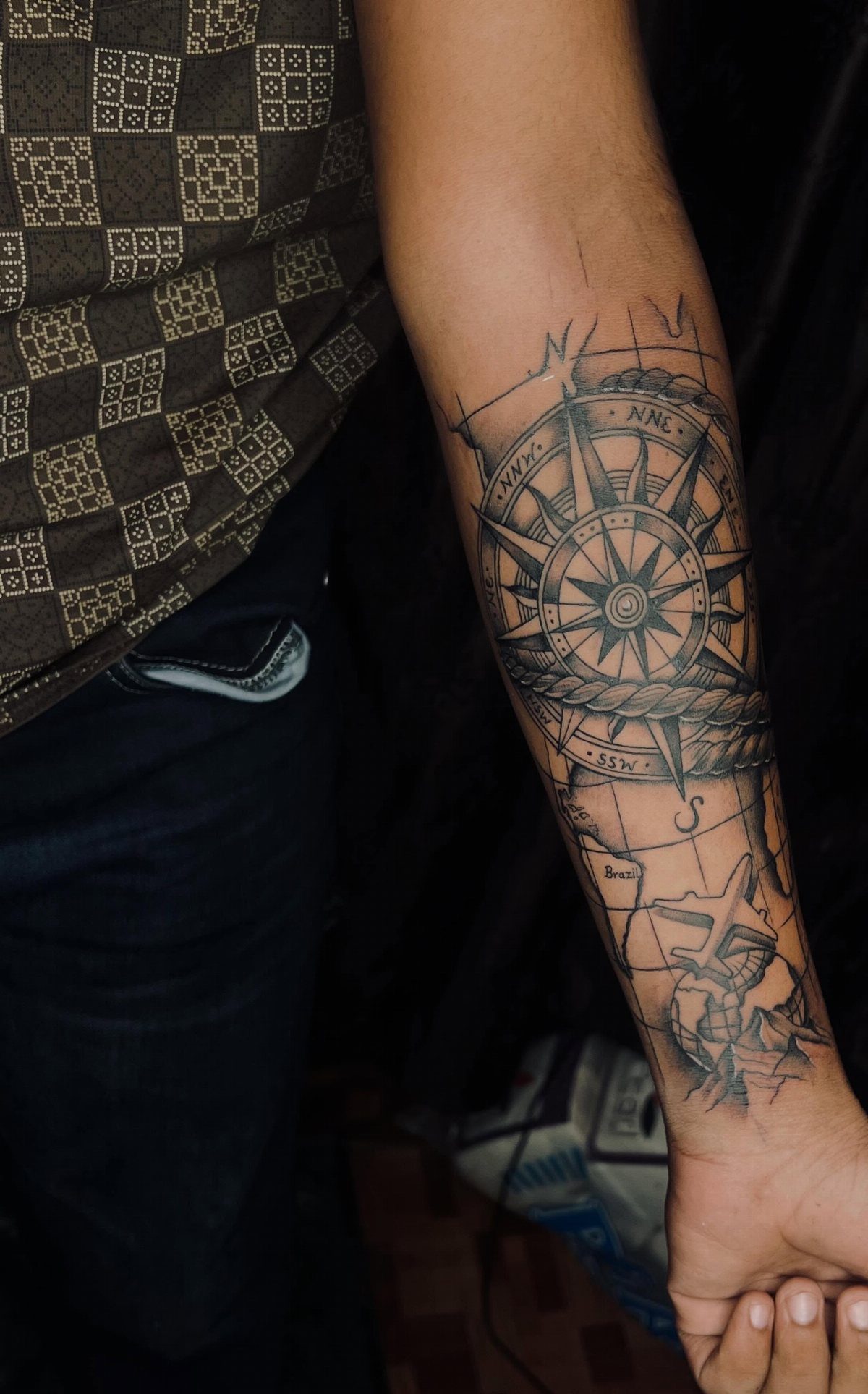 A detailed black ink nautical compass tattoo on a person's forearm with map elements.