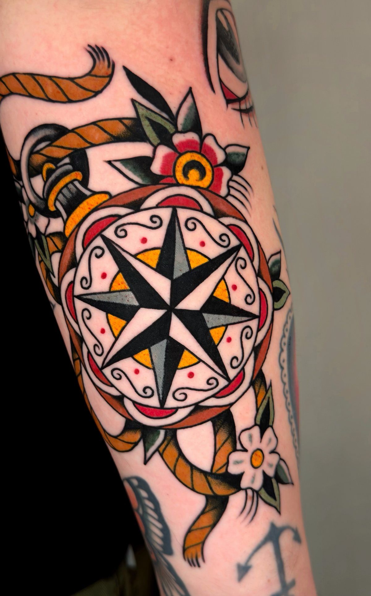 A colorful traditional tattoo of a compass rose with rope and flowers on a person's arm.