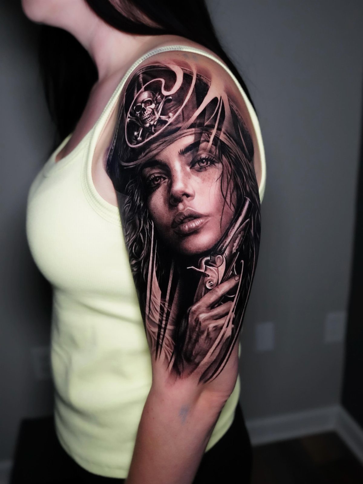 A realistic black and grey tattoo of a female pirate on a person's shoulder.