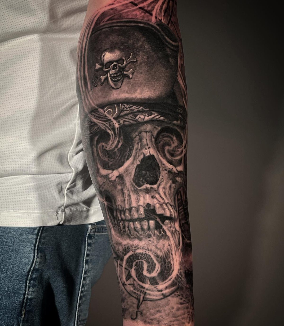 A detailed black and grey tattoo of a pirate skull wearing a tricorn hat on an arm.