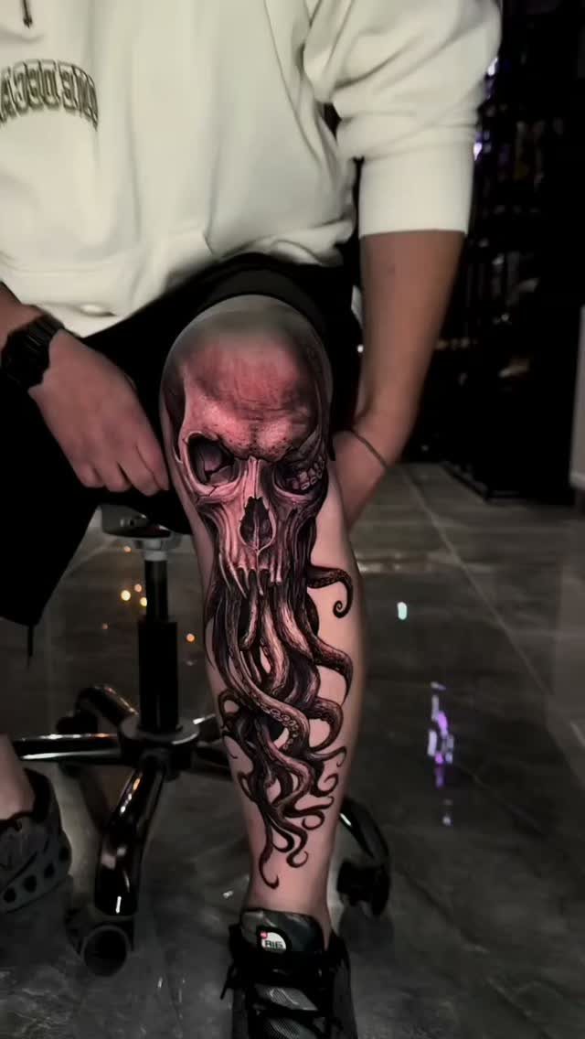 A large black and grey tattoo of a skull merged with octopus tentacles on a person's leg.