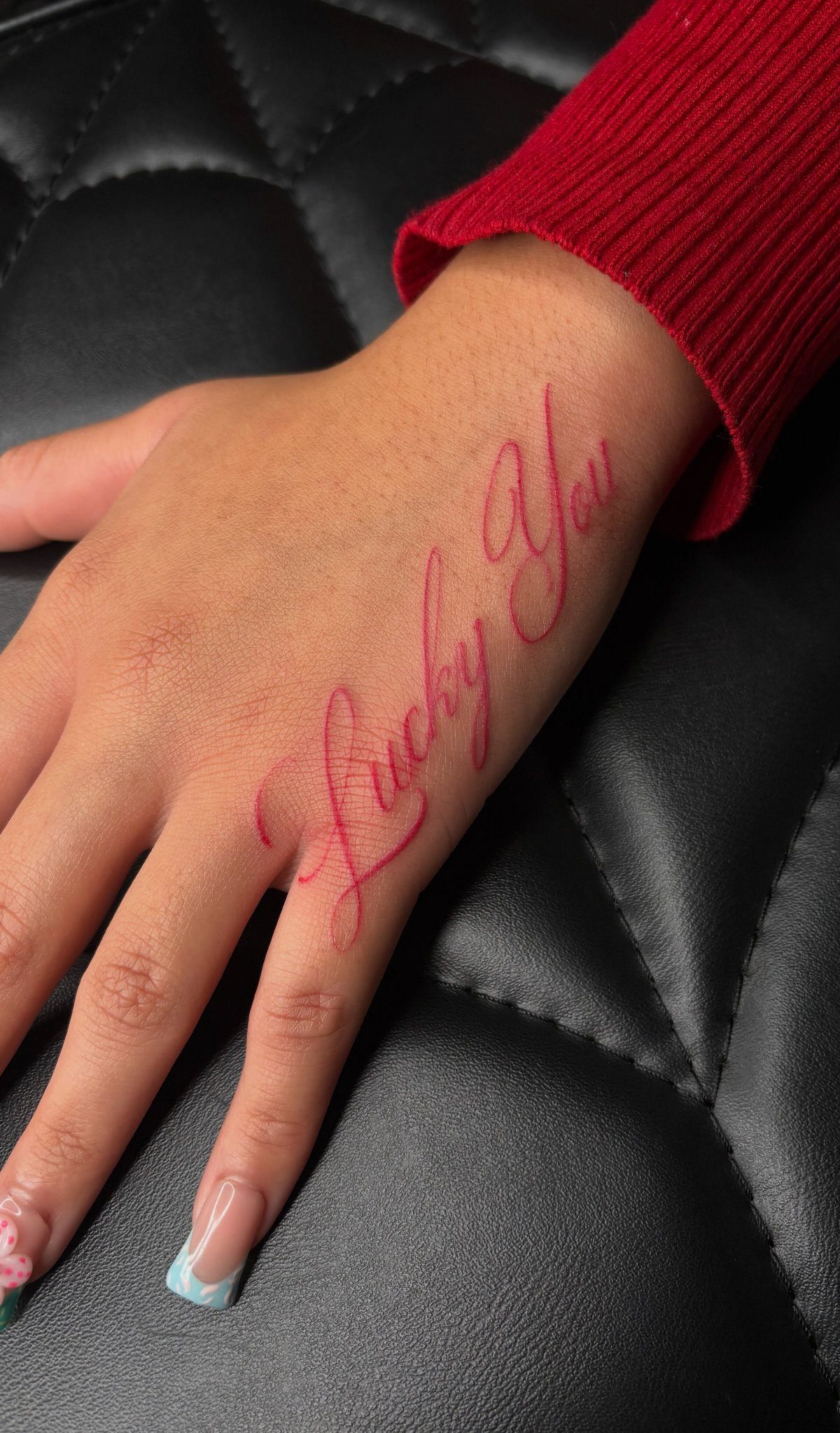 8 Red Fine Line Tattoo Ideas for Minimal Statement 1 A hand with a red fine line cursive tattoo reading Lucky You on the skin.