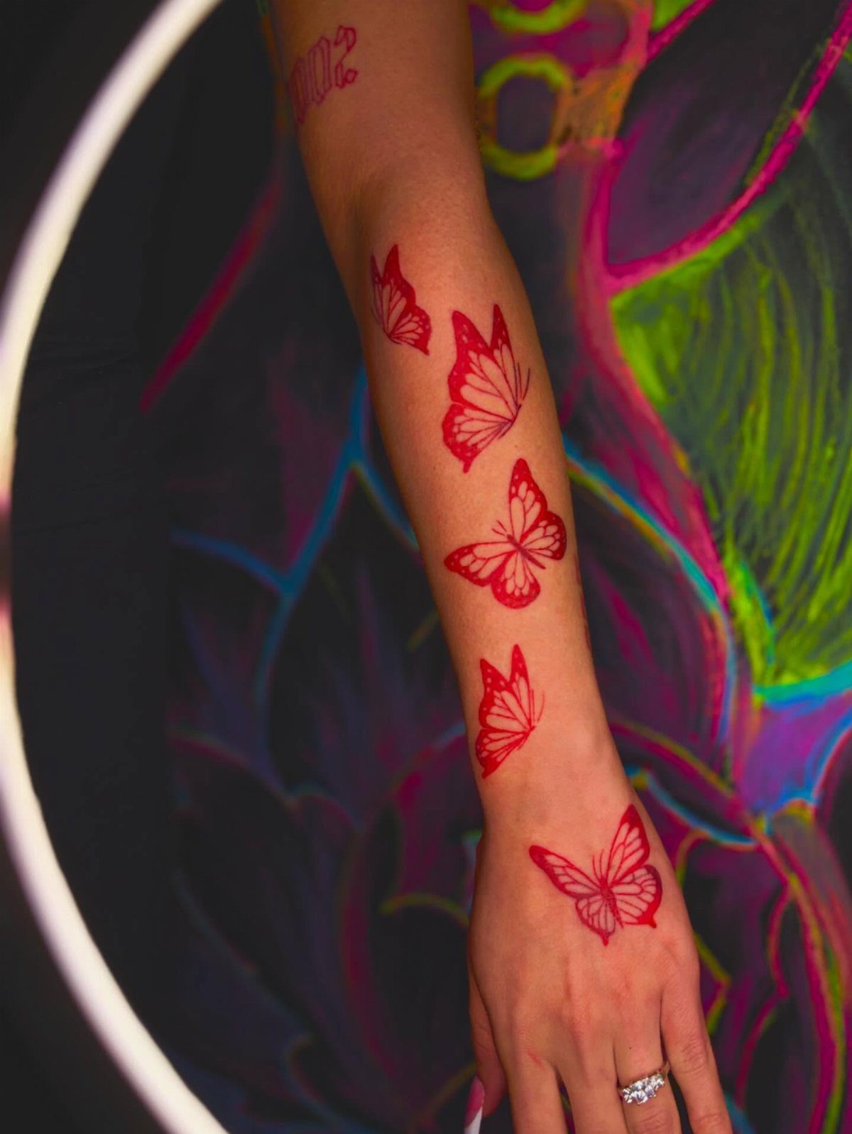 8 Red Fine Line Tattoo Ideas for Minimal Statement 4 A person's arm decorated with several small red fine line butterfly tattoos.