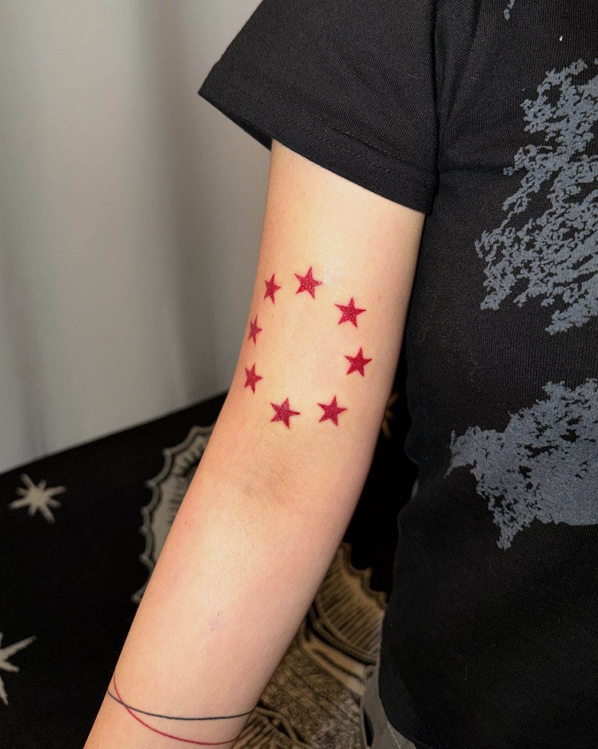 8 Red Fine Line Tattoo Ideas for Minimal Statement 6 A circular arrangement of small red star tattoos on a person's upper arm.