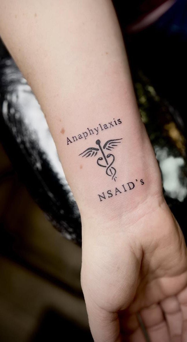 Sickness Tattoo Ideas: 6 Designs That Mean Something 5 A black ink tattoo on a person's wrist featuring a caduceus and medical text.