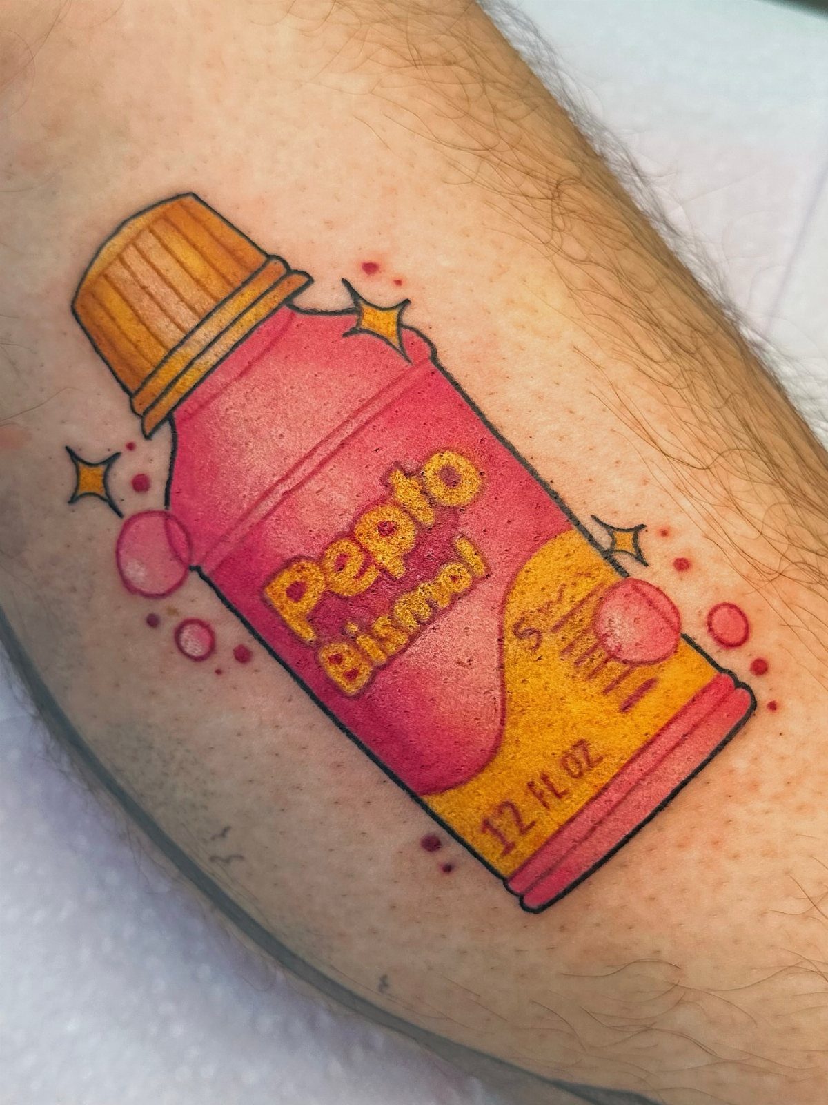 Sickness Tattoo Ideas: 6 Designs That Mean Something 6 A colorful tattoo of a pink Pepto Bismol bottle on a person's leg.