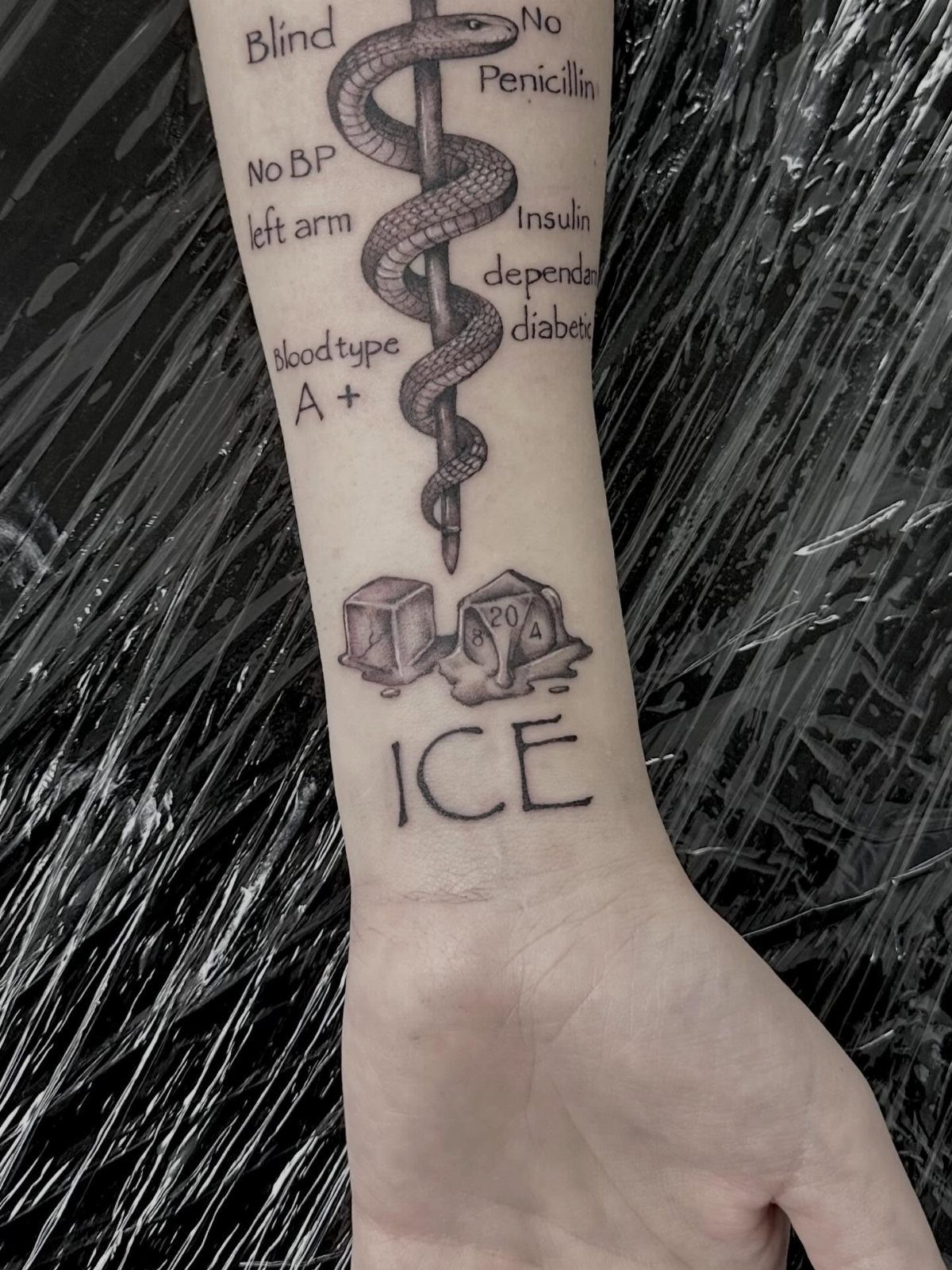 Sickness Tattoo Ideas: 6 Designs That Mean Something 2 A forearm tattoo featuring medical information, a caduceus symbol, dice, and the word ICE in black ink.