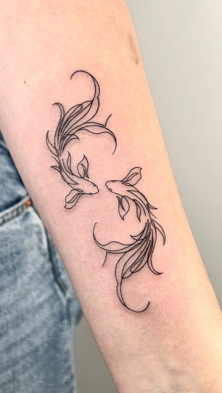 Two black ink fine-line fish tattoos with long flowing fins on a person's forearm.