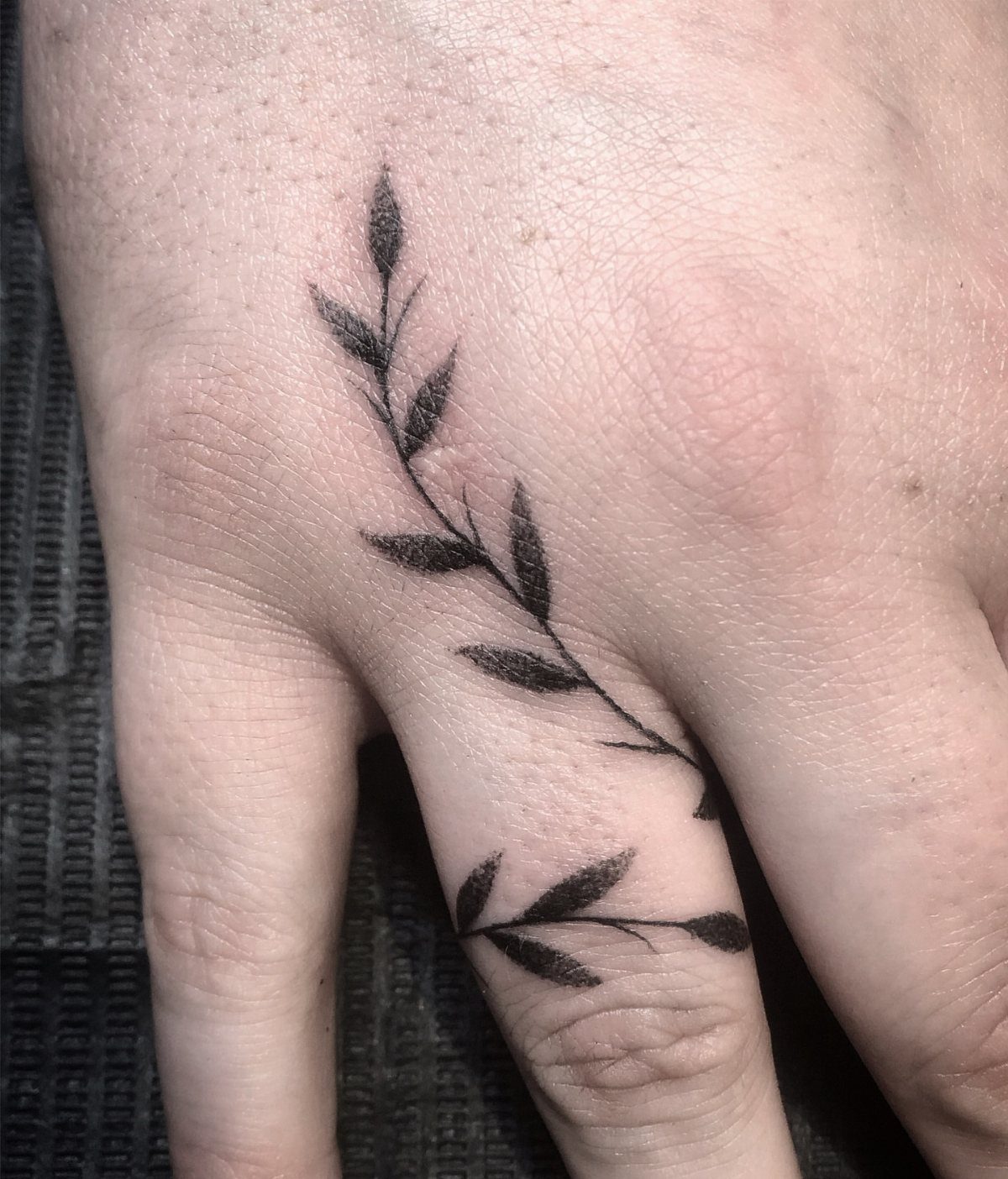 Black ink leaf branch tattoos on a person's hand and finger.